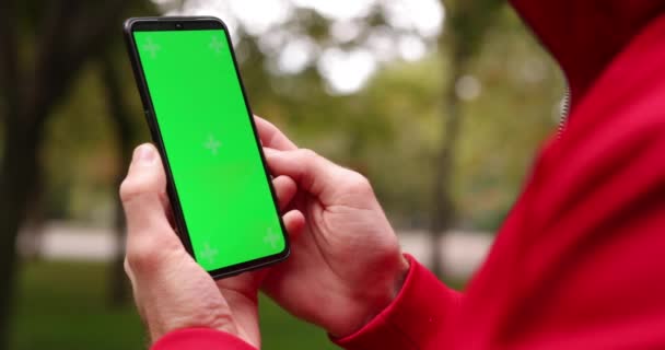 Hombre sosteniendo la pantalla verde del teléfono inteligente en un parque — Vídeos de Stock