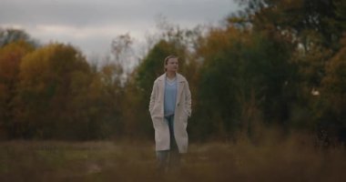 Trençkotlu bir kadın sonbahar ormanında yürüyor zevkle, ağır çekimde.