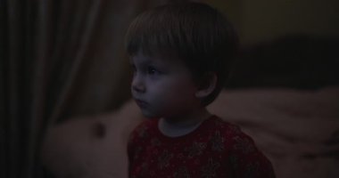 Karanlık bir odada televizyon izleyen küçük bir çocuk.