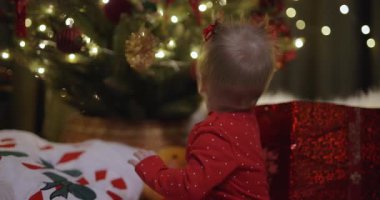 Yeni yıl tatilinde Noel ağacının yanında oturan küçük bir kız top oynuyor.