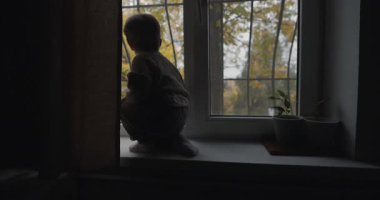 Pencereden dışarı bakan küçük bir çocuk. Sonbahar açık havada..