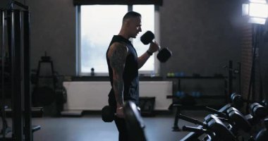 Kol egzersizi yapan bir adam spor salonunda kollarını sallıyor.