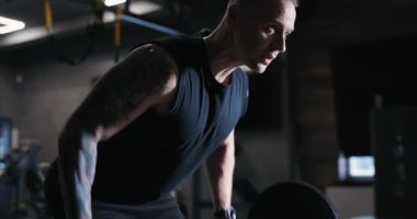 Eğilip halterli sıra egzersizi yapan bir adam spor salonunda kaslarını pompalıyor.