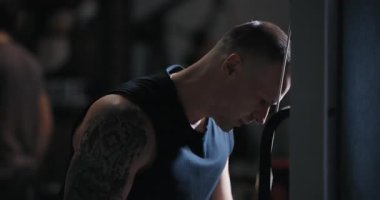 Spor salonunda kollarını sallayan antrenman aletleri üzerinde triseps egzersizi yapan bir adam.