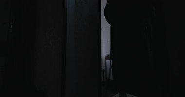 Çıplak bir adamın silueti bornozunu çıkarıp banyoya giriyor.