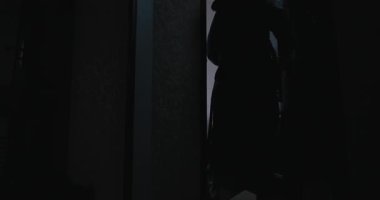 Çıplak bir adamın silueti bornozunu çıkarıp banyoya giriyor.