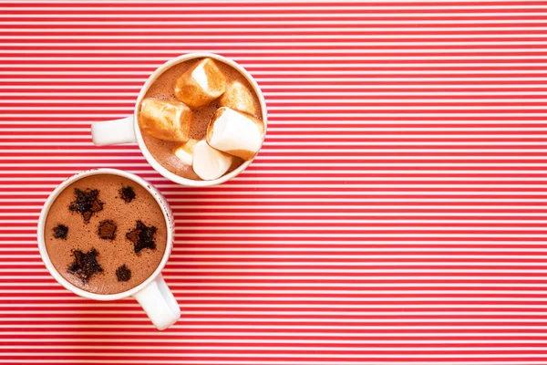 White cups with hot cocoa and marshmallows and cocoa powder decor stars shape on winter holidays red white striped background with copy space, horizontal