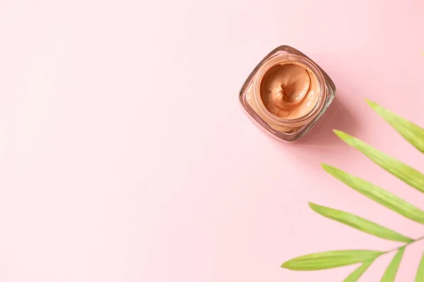 Facial pink clay mask for sensitive skin and defocused tropical leaf on pink background with copy space, top view. Skin care beauty delicate detox product horizontal format banner
