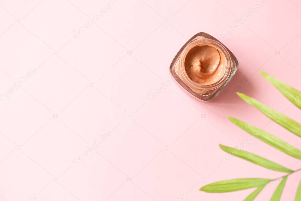 Facial pink clay mask for sensitive skin and defocused tropical leaf on pink background with copy space, top view. Skin care beauty delicate detox product horizontal format banner