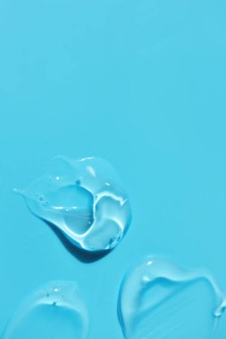 Mavi arkaplanda fotokopi alanı ve dikey makroyla şeffaf temiz jel temizleyici ya da dezenfektan örneği. Aloe veralı kozmetik serumu, hyaluronik asit lekeli.
