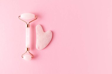 Pembe kuvars yüz silindiri ve gua sha, üst manzara. Pembe arka planda moda yüz masajı araçları