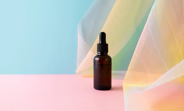 Serum kahverengi cam kavanoz üzerinde pipeti mavi pembe arka planda renkli gökkuşağı organza balık ağları kumaş örtüsü