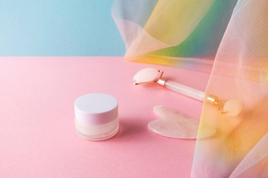 Nem kremi, kuvars yüz silindiri ve mavi arkaplan rengarenk gökkuşağı örtüsüne yapılan cilt masajı için gua sha.