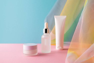 Serum, yüz temizleyici, mavi arkaplanda nemlendirici krem renkli gökkuşağı organza balık ağları kumaş örtüsü