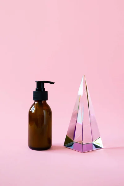 Fles met pomp voor beauty product mockup en glazen piramide prisma op roze achtergrond met kopieerruimte, verticaal. Cosmetisch product trendy minimalisme — Stockfoto