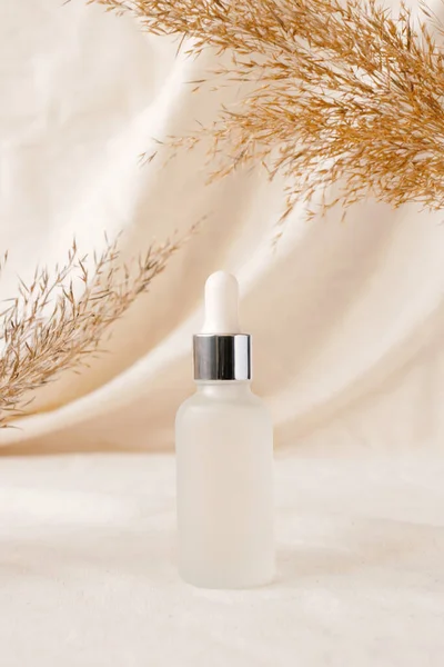 Serum fles schoonheid product mockup op linnen draperieën en droge tak van weide plant. Onderwerp eco biologische cosmetica met natuurlijke extracten. Zwijg. — Stockfoto