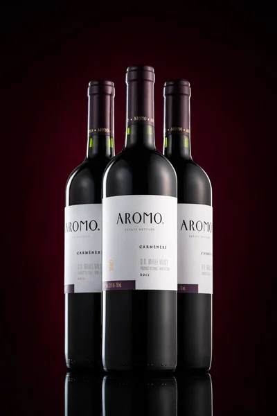 Три пляшки Aromo Карменер червоного вина на чорному тлі з фіолетовим пляма. — стокове фото