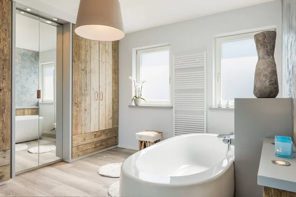 Modernes Badezimmer mit separater Badewanne, großem Spiegel und Holzboden. Stockbild