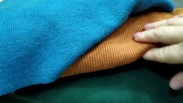 Het meisje kiest voor gebreide stoffen op basis van hun eigenschappen. Warme geweven gebreide kleding. Gebreide truien gevouwen in een stapel. — Stockvideo