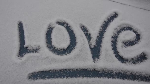 Η λέξη αγάπη είναι γραμμένη στο παράθυρο του αυτοκινήτου. Μια ασυνήθιστη δήλωση αγάπης. Χιονισμένο χαιρετισμούς χειμώνα για την ημέρα του Αγίου Βαλεντίνου — Αρχείο Βίντεο