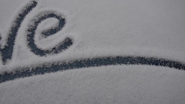 La palabra amor está escrita en la ventana cubierta de nieve del coche. Una inusual Declaración de amor. Saludos de invierno en San Valentín — Vídeos de Stock