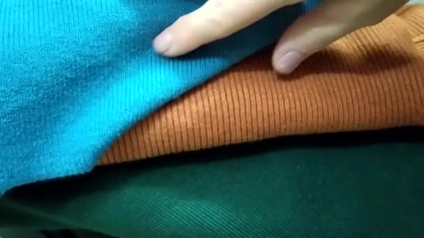 Prendas de punto de textura cálida. La niña elige tejidos de punto de acuerdo a sus propiedades. Suéteres de punto doblados en una pila. — Vídeos de Stock