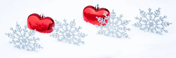 Karda bir çift kalp ve kar tanesi. Kırmızı kalpli, karlı bir Noel arkaplanı. Noel panoramik arka planı.