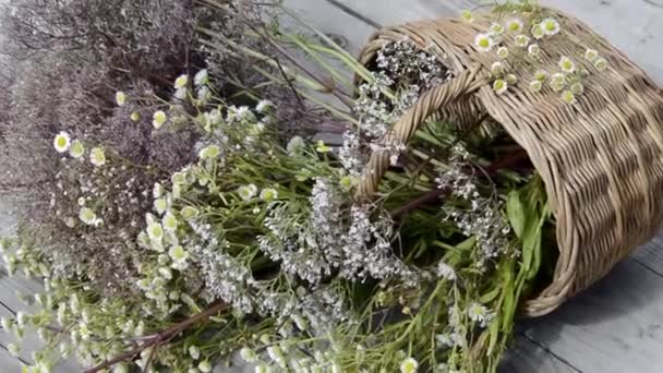 Een boeket wilde bloemen in een rieten mandje ligt op een houten achtergrond. Lichte wind. Zomer schilderachtig boeket. Grasveld van bloeiende kruiden op een zonnige dag. — Stockvideo