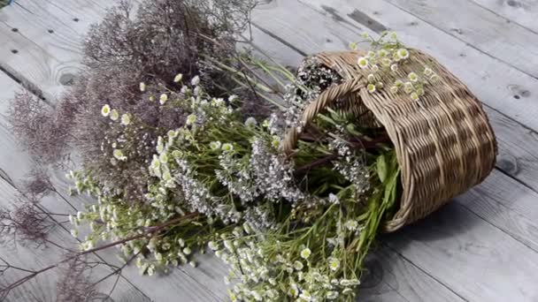 A bouquet of wild flowers in a wicker basket lies on a wooden background. Light wind. Meadow of flowering herbs on a sunny day. Summer scenic bouquet. — Stock Video