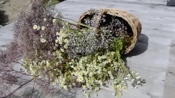 Een boeket wilde bloemen en gedroogde bloemen in een rieten mandje ligt op een houten achtergrond. Lichte wind. Grasveld van bloeiende kruiden op een zonnige dag. Zomer schilderachtig boeket. — Stockvideo