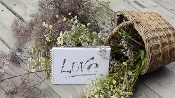 Declaração de amor no fundo de flores silvestres em uma cesta de vime. Prado de ervas com flores em um dia ensolarado. Buquê cênico de verão. — Vídeo de Stock