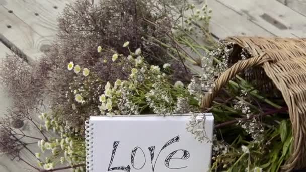Declaração de amor no fundo de flores silvestres em uma cesta de vime. Prado de ervas com flores em um dia ensolarado. Buquê cênico de verão. Cartão postal do amor. — Vídeo de Stock