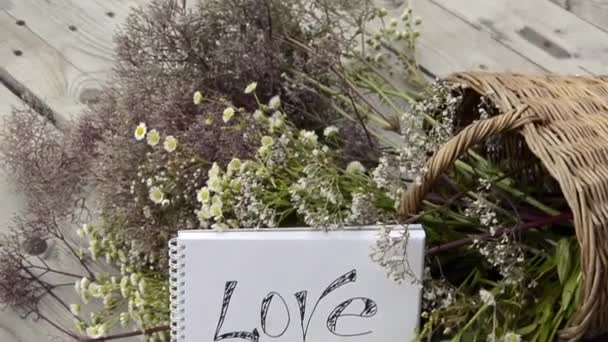 Cartolina d'amore. Dichiarazione d'amore sullo sfondo di fiori di campo in un cesto di vimini. Prato di erbe fiorite in una giornata di sole. Bouquet panoramico estivo. — Video Stock