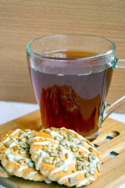 Cookies and a cup of tea for breakfast. View from above. Fragrant pastries with sunflower seeds next to strong tea in a glass close-up. Vertical background.