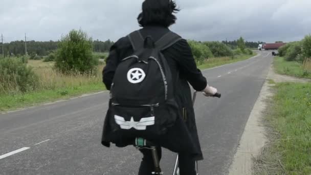 Siyah yağmurluklu kız dışarıda bisiklete biniyor. Bisikletçi pist boyunca sürüyor. Doğada bisiklet sürmek. 2020 yazında Rusya. Editör ağır çekim videosu. — Stok video