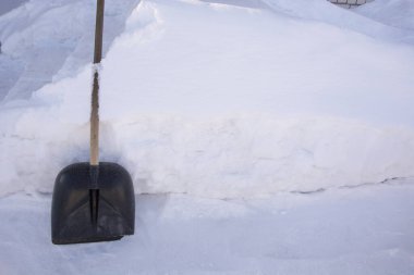 Kar küreği yüksek bir kar yığınına karşı duruyor. Evin etrafındaki karları temizleyin. Kışın bahçede çok kar vardır..