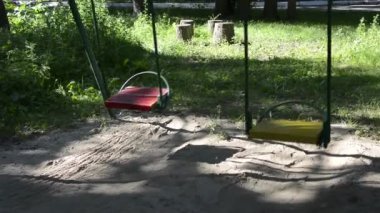 Empty swing during a pandemic. In the city park, the mystical swinging of a children's swing on chains on a summer evening. The ghost is swinging the swing on the playground.