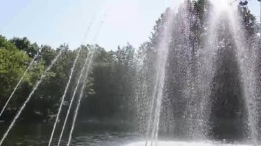 Yazın şehir parkında eski bir çeşme. Çeşmeden fışkıran su gölün içine düşer..