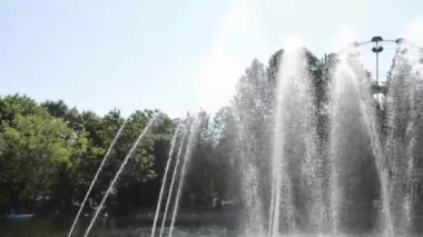 Çeşmeden gelen su fıskiyeleri, Ferris halkasının arka planında parlıyor. Yazın şehir parkında eski bir çeşme.