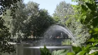 Çeşmeden gelen su fıskiyeleri güneşte parlıyor. Yazın şehir parkında eski bir çeşme.