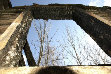 Evi yakmışlar. Yıkılan bir binanın penceresinden mavi gökyüzüne ve beyaz bulutlara bakıyoruz. Kömürleşmiş günlükler.