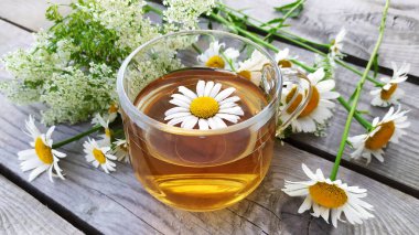 Ahşap bir arka planda cam bir fincanda papatya aromalı çay. Yaz aylarında kır çiçekleri ve papatya çayı ile dolu bir hayat. Çiçek arka planı.