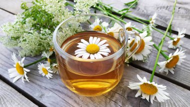 Ahşap bir arka planda cam bir fincanda papatya aromalı çay. Yaz aylarında kır çiçekleri ve papatya çayı ile dolu bir hayat. Çiçek arka planı.