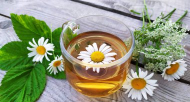 Camdan bir fincanda, ahşap bir arka planda papatya çayı. Çiçek arkaplan. Yaz aylarında kır çiçekleri ve şifalı papatya çayı ile hayat devam ediyor..