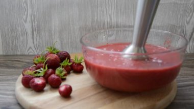 Bahçe çilekleri. Elektrikli blender ile çırpılmış çilekli meyve suyu. Cam bir tabakta taze olgun çilekler, yanında da tahtadan bir çilek var..