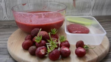 Konteynırlarda kış için çilekli püre hazırlığı. Cam bir tabakta blender ile çırpılmış olgun çilekler, hemen yanında ahşap bir tahtanın üzerinde bir böğürtlen yatıyor..