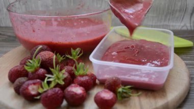 Kışın konteynırlarda çilek toplamak. Cam bir tabakta blender ile çırpılmış olgun çilekler, hemen yanında ahşap bir tahtanın üzerinde bir böğürtlen yatıyor..