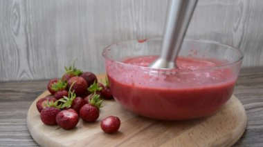 Elektrikli blender ile çırpılmış çilekli meyve suyu. Kış için çilek topluyorum. Taze olgun çilekler cam bir tabağın içinde, yanında bütün bir böğürtlen duruyor..