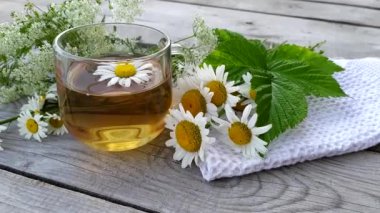 Papatya çayı yakın. Cam bir fincandaki şifalı yaz içeceği ahşap bir arka planda duruyor. Vahşi papatya çiçekleri kaynar suda demlenir..