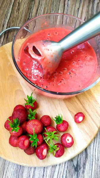 Elektrikli blender ile olgun çilekli smoothie yapıyorum. Bir kase böğürtlen püresi ve tüm böğürtlen kesim tahtasının üzerinde..